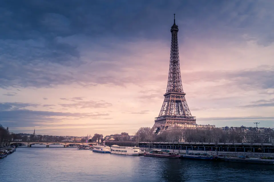 The Eiffel Tower seen across the Seine under a pink and violet sky