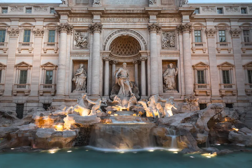 The Trevi Fountain in Rome lit at dusk, its sculpted figures above the basin